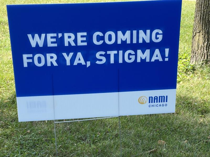 A blue sign on grass with the words 'We're coming for ya, Stigma!' in white. In the lower left of the sign is the logo for NAMI Chicago
