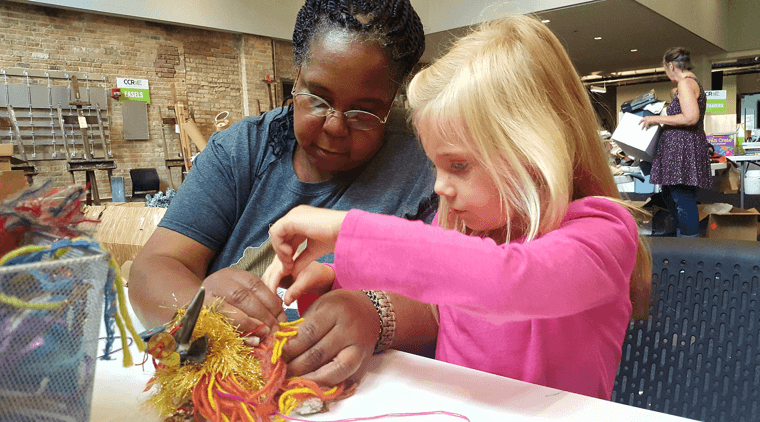 Black older woman guiding a young Caucasian girl in an art project
