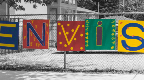 Colorful painted sign saying, "Envision" hanging outside on a fence on a snowy day