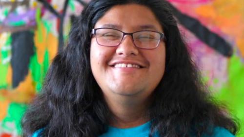 Close up photo of person's face smiling and standing in front of a painted colorful background