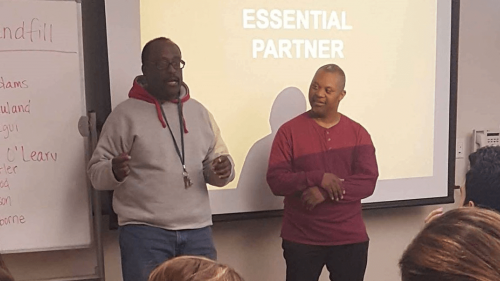 Teacher and student stranding in front of a class by the projection screen and white board