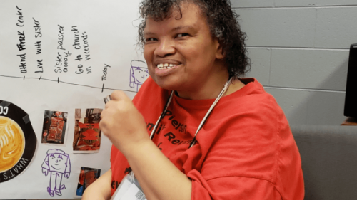 Woman of color sitting in front of a timeline, wearing a red t-shirt and smiling