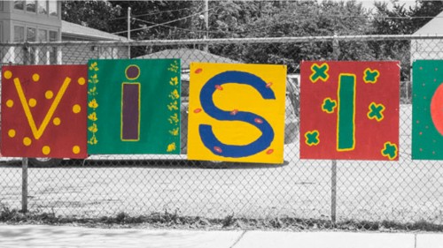 Colorful painted sign saying, "Envision" hanging outside on a fence on a snowy day