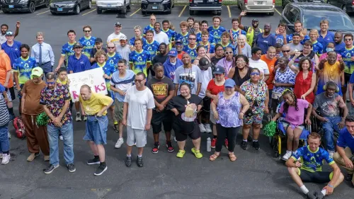 Large diverse group of over 100 people wearing blue 'Journey of Hope' shirts gathered in a parking lot, smiling and waving at the camera.