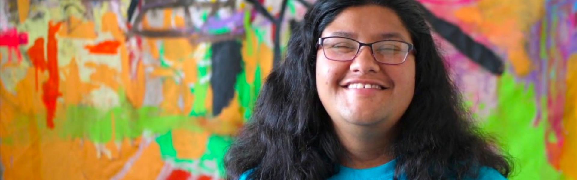 Close up photo of person's face smiling and standing in front of a painted colorful background