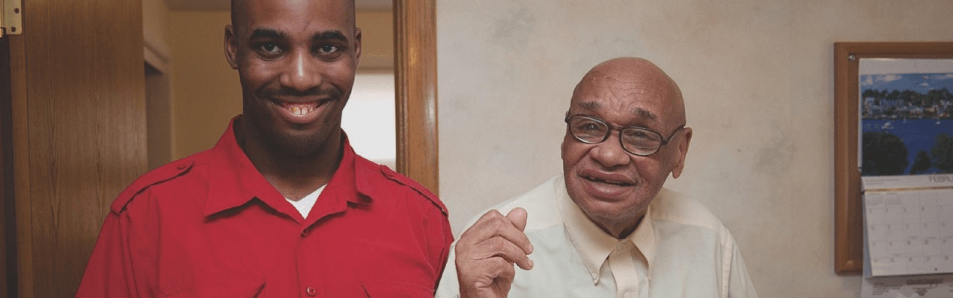 A young black man standing inside next to an older black man and smiling