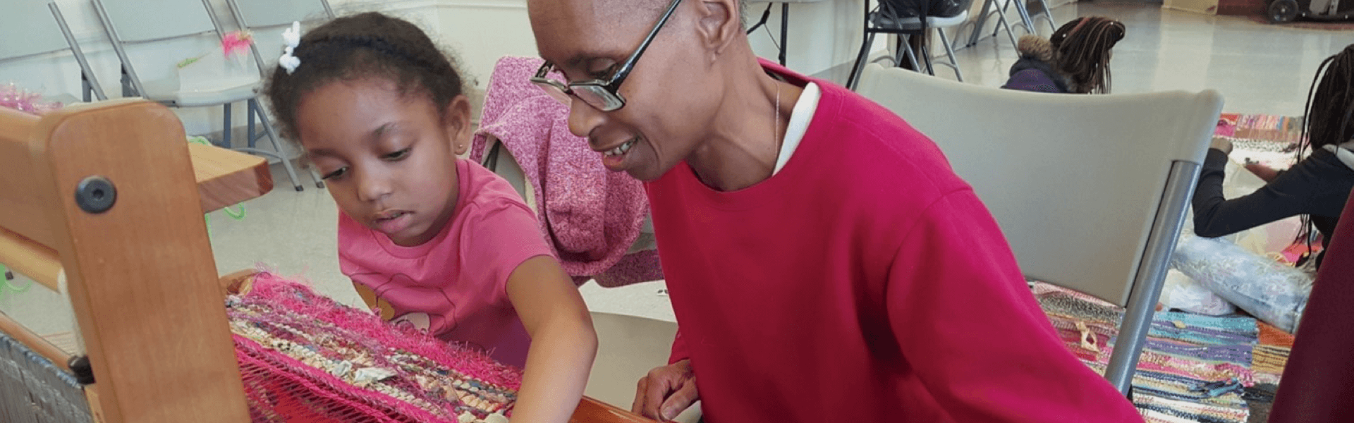 Woman of color and young girl sitting and weaving together