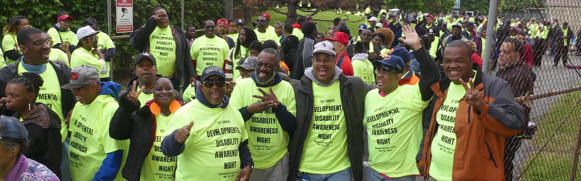 Large group of black men and women standing outside and wearing "developmental disability awareness night" t-shirts