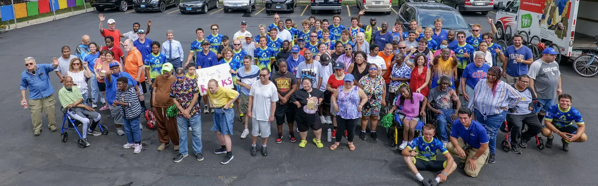 Large diverse group of over 100 people wearing blue 'Journey of Hope' shirts gathered in a parking lot, smiling and waving at the camera.