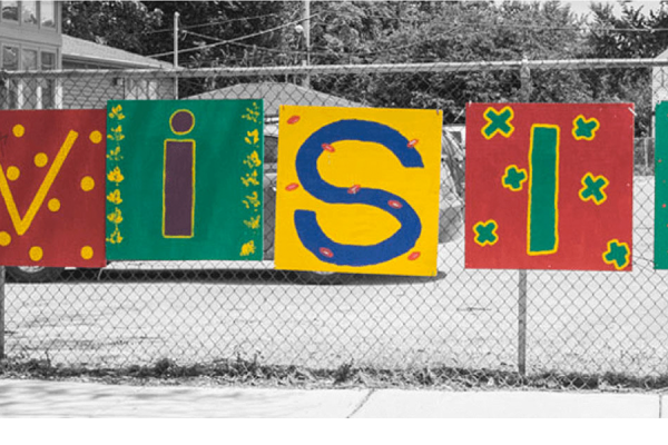 Colorful painted sign saying, "Envision" hanging outside on a fence on a snowy day