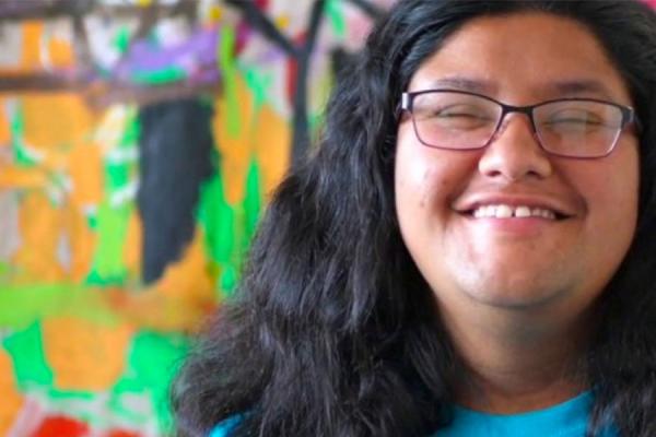 Close up photo of person's face smiling and standing in front of a painted colorful background