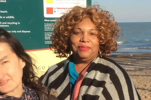 Two women standing by a beach with a green informational sign behind them.