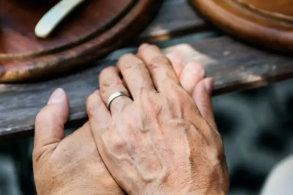 Close-up of hands with a silver ring resting on a wooden table.