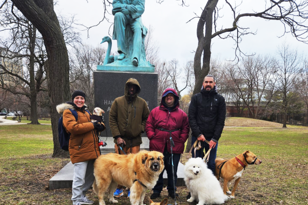 A group of people walking dogs stand in front of a statue in a park.