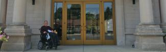 a man sits in an electric wheelchair outside the entrance of a bank with a stone facade