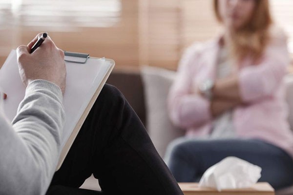 ack view of psychotherapist writing notes, assessing patient's health and giving diagnosis to a woman sitting on a couch in the blurred background during counseling session stock photo. Image by KatarzynaBialasiewicz