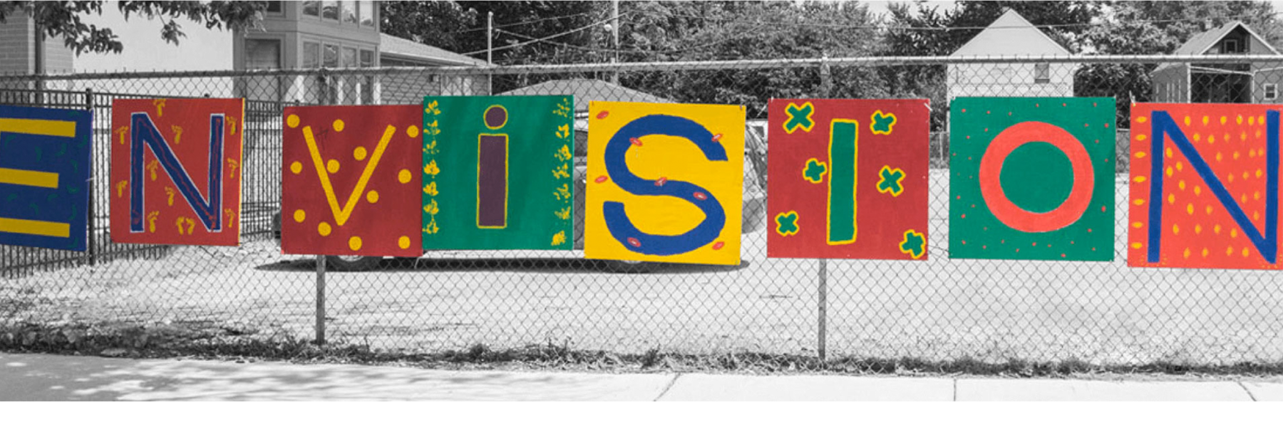 Colorful painted sign saying, "Envision" hanging outside on a fence on a snowy day