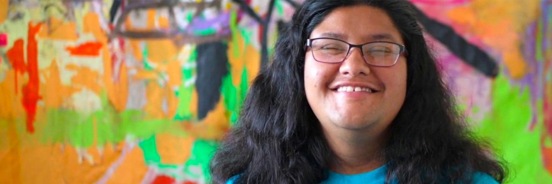 Close up photo of person's face smiling and standing in front of a painted colorful background