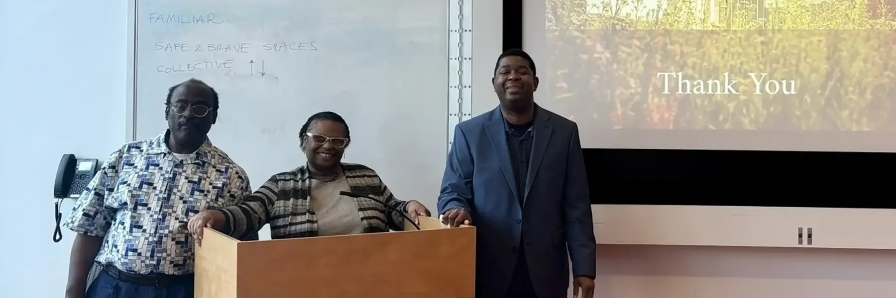 Three people stand by a podium and presentation screen with 'Thank You' displayed.