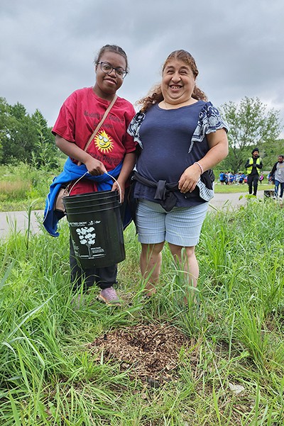 Jessica and Ruth water a sapling.