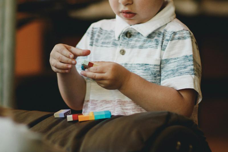 A child in a white and grey striped polo shirt plays with colorful blocks.