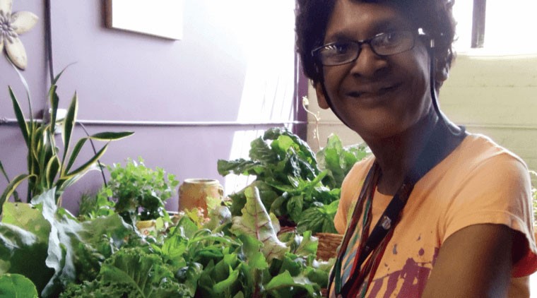 Woman of color wearing an orange shirt and smiling while standing next to plants
