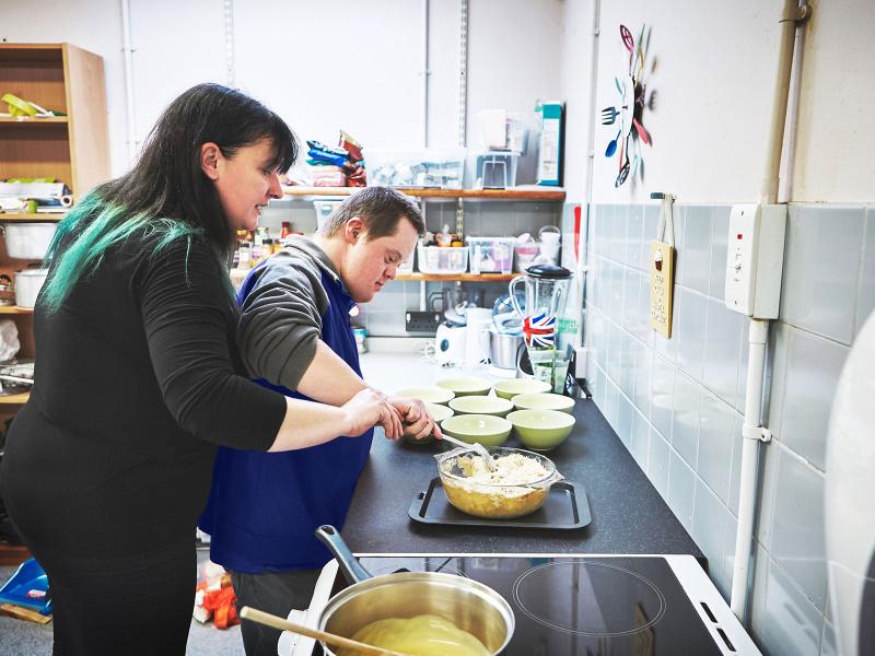 Two people in a kitchen mixing ingredients, surrounded by cooking utensils and bowls.