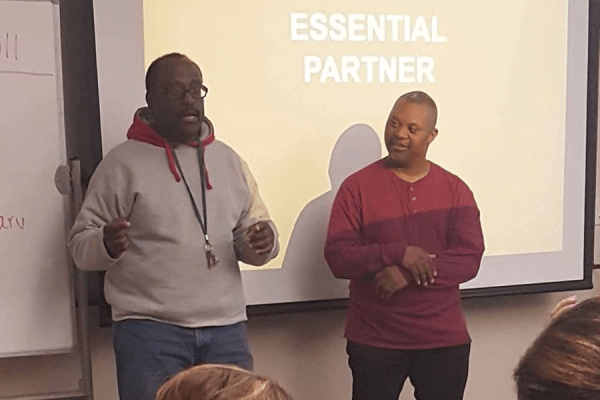 Teacher and student stranding in front of a class by the projection screen and white board