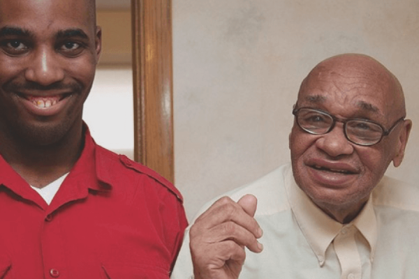 A young black man standing inside next to an older black man and smiling