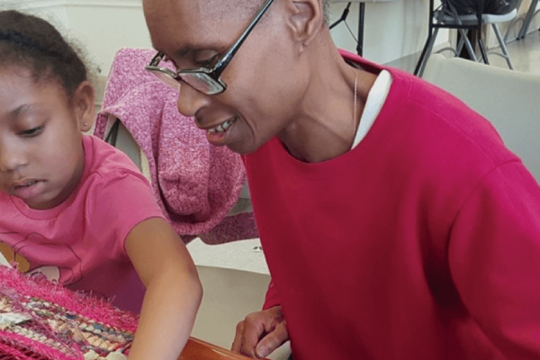 Woman of color and young girl sitting and weaving together